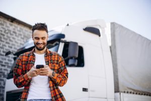 Homem sorrindo olhando para celular ao lado de caminhão